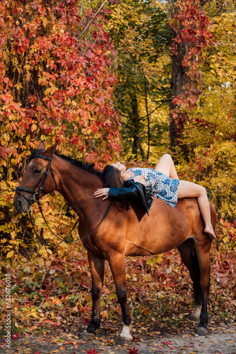 A beautiful young brunette kisses a horse. Autumn forest. Love for animals