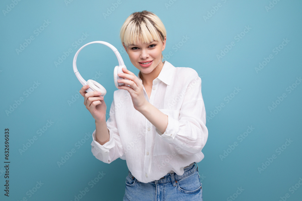 young successful pretty blond office worker woman in a white shirt and jeans uses headphones during a break. business concept young successful pretty blond office worker woman in a white shirt and jeans uses headphones during a break. business concept