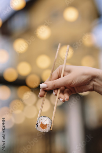 a woman's hand holds a salmon roll on chopsticks with flashlights in the background