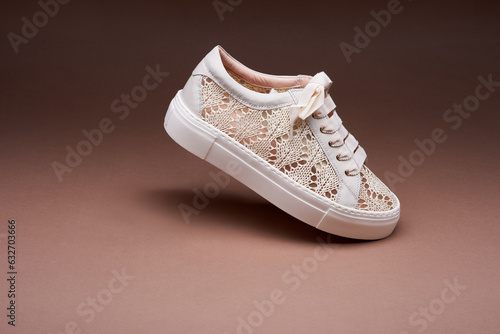 Side view of stylish beige knitted design sneaker with a white thick rubber sole on a gradient brown background at an angle and inclination. The concept of modern footwear