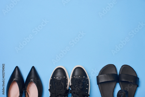A set of modern black women's shoes on a pastel blue background with copy space on top and center. Stylish pumps, sneakers and sandals. Flat lay, top view. Creative fashion photography