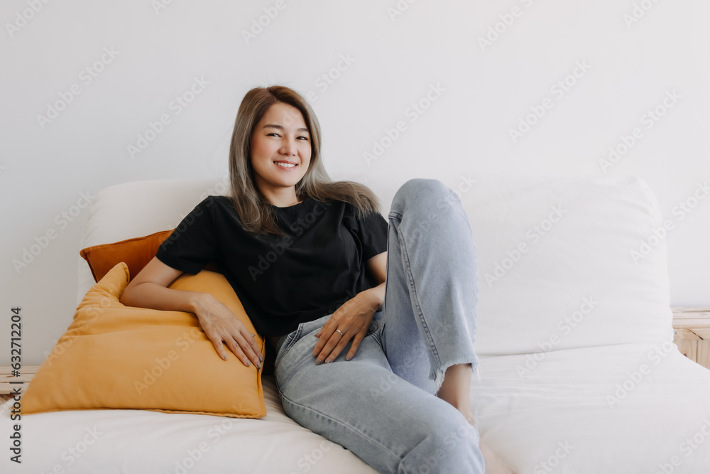 Fototapeta premium Happy asian woman sits and relax on sofa in one good fine day.