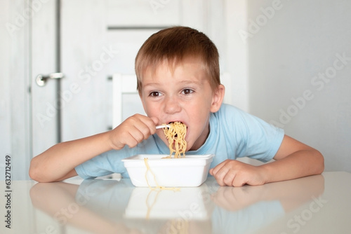 Happy preschool child eats spaghetti pasta. Boy in kitchen at table eating noodles. Concept of baby food. Enjoy your meal