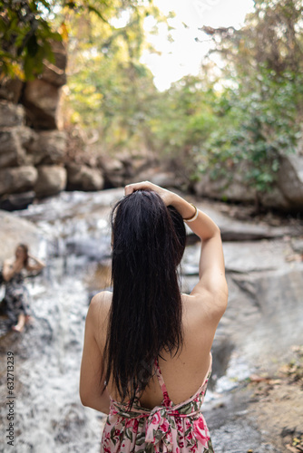 young women tourist in vintage dress stands alone on rock by waterfall in the forest hoping to cool down for swim. The back of young Asian women tourist who enjoys playing in waterfall alone. © thatinchan