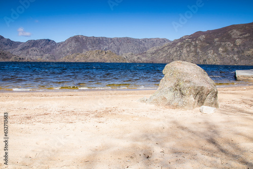 White sand beach of Lake Sanabria with a large rock, blue waters and large mountains in the background. Viquela beach. Sanabria Natural Park photo