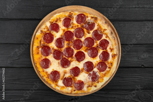 Top view of hot pepperoni pizza on black wooden background, flat lay.