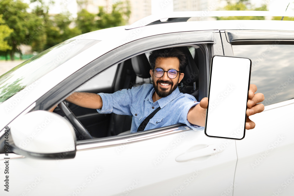 Smiling young eastern man sitting in auto, showing phone Smiling young eastern man sitting in auto, showing phone