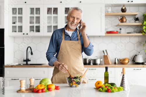 Wallpaper Mural Smiling senior man talking on cellphone while cooking in kitchen interior Torontodigital.ca