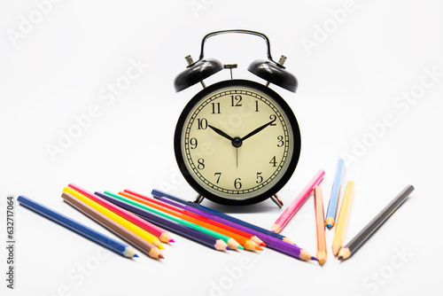 alarm clock with color pencils on yellow background
