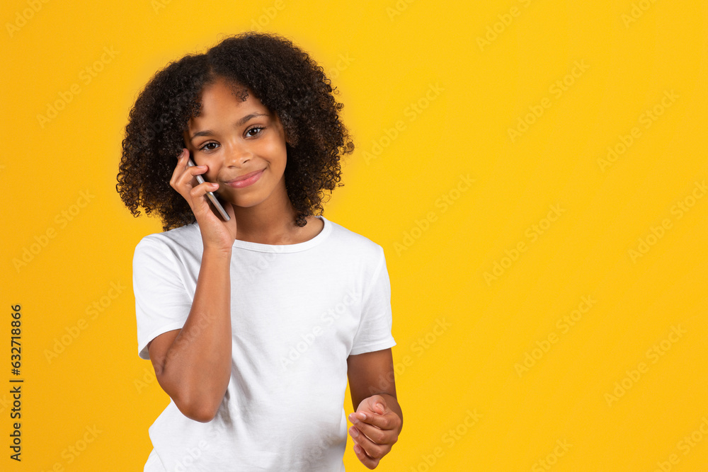 Happy teenage black pupil girl in white t-shirt calling by phone, isolated on yellow background, studio Happy teenage black pupil girl in white t-shirt calling by phone, isolated on yellow background, studio