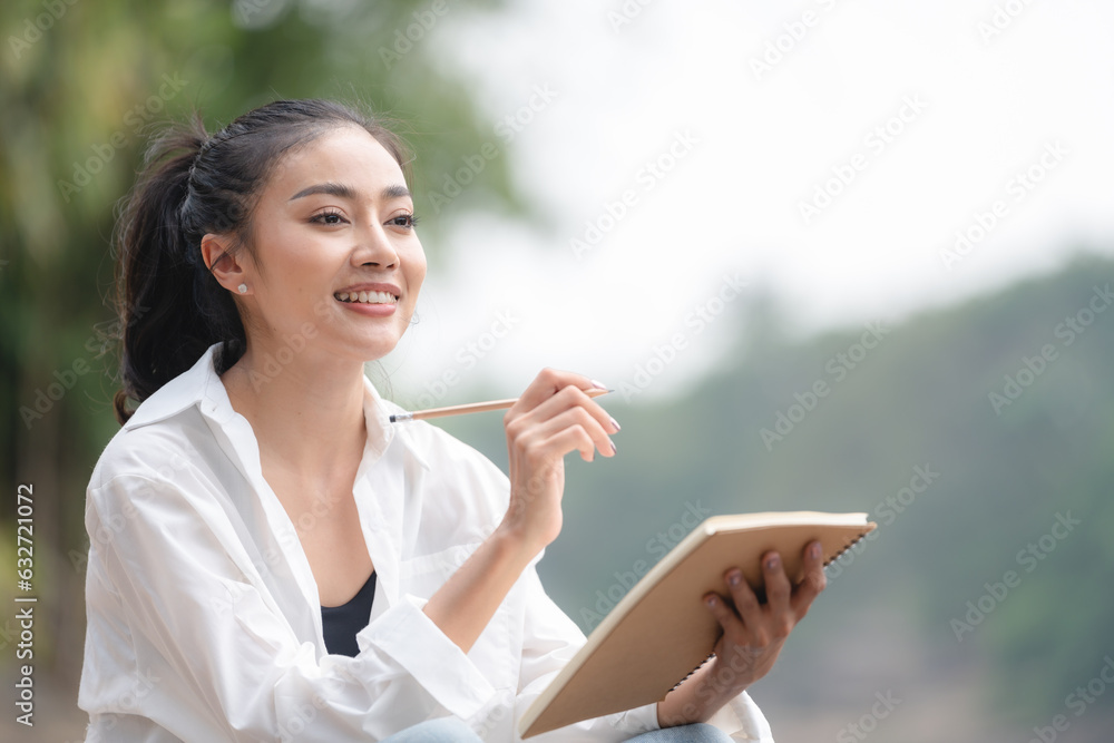 Photo of young attractive Asian woman writing on diary while sitting outdoors in the park, Writer sitting in garden, Female freelance are relaxing to writing story on jobs, beautiful Asian women Photo of young attractive Asian woman writing on diary while sitting outdoors in the park, Writer sitting in garden, Female freelance are relaxing to writing story on jobs, beautiful Asian women