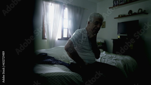 Thoughtful senior man pondering decision while sitting by bedside in somber room with hand in chin contemplating life in moody lonely scene