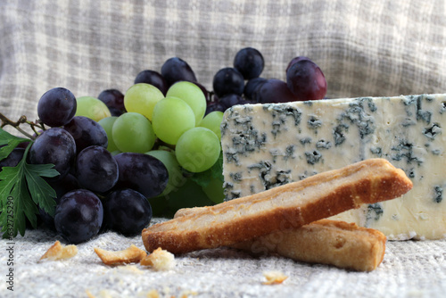 Gourmet photo with rotten cheese, green and dark grapes, and cheese sticks.