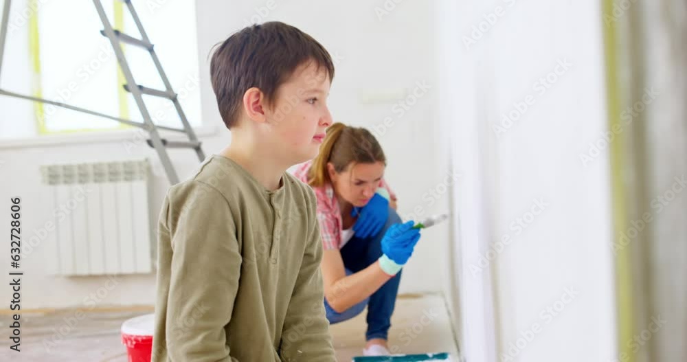 Happy family mother and son paint the wall with paint using roller and brush Happy family mother and son paint the wall with paint using roller and brush