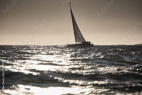 The view of sailboat is heeling at sunset, reflection of sun on water surface