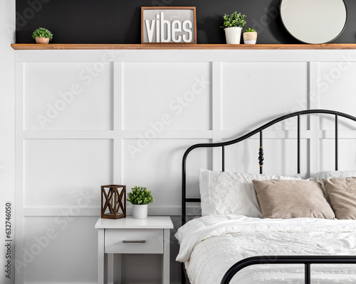 Canvas Print A farmhouse bedroom detail shot with wainscoting, decorations on a natural wood shelf with black paint above, and a black metal bed frame