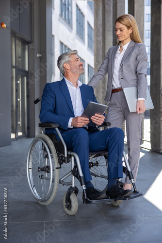 Business partners with adult gray haired man in wheelchair talking outdoors.