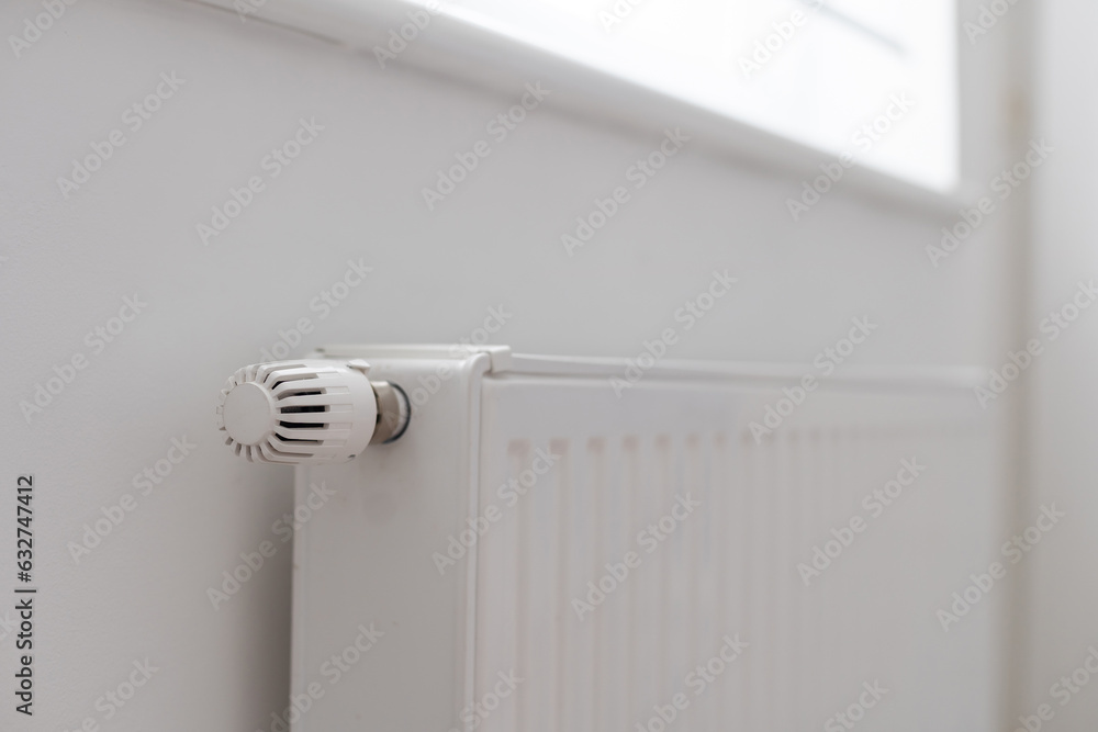 A steel panel heating radiator is placed under the windowsill on a white wall. A steel panel heating radiator is placed under the windowsill on a white wall.