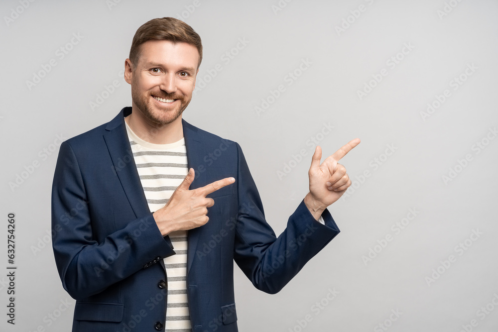 Smiling businessman points with index fingers on empty space for ad on gray studio background. Confident happy middle age promoter man looking at camera showing by forefinger at blank copy space. Smiling businessman points with index fingers on empty space for ad on gray studio background. Confident happy middle age promoter man looking at camera showing by forefinger at blank copy space.