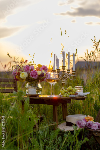 Table decorated with chandelier. Wineglasses with white wine. Sunset, summer, golden hour. Perfect surprise date for loving couple. Beautiful romantic outdoor wedding decor in a field