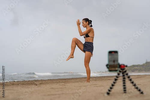 beautiful sports girl brunette blogger trains on the sand on the seashore takes pictures of herself on a mobile phone.