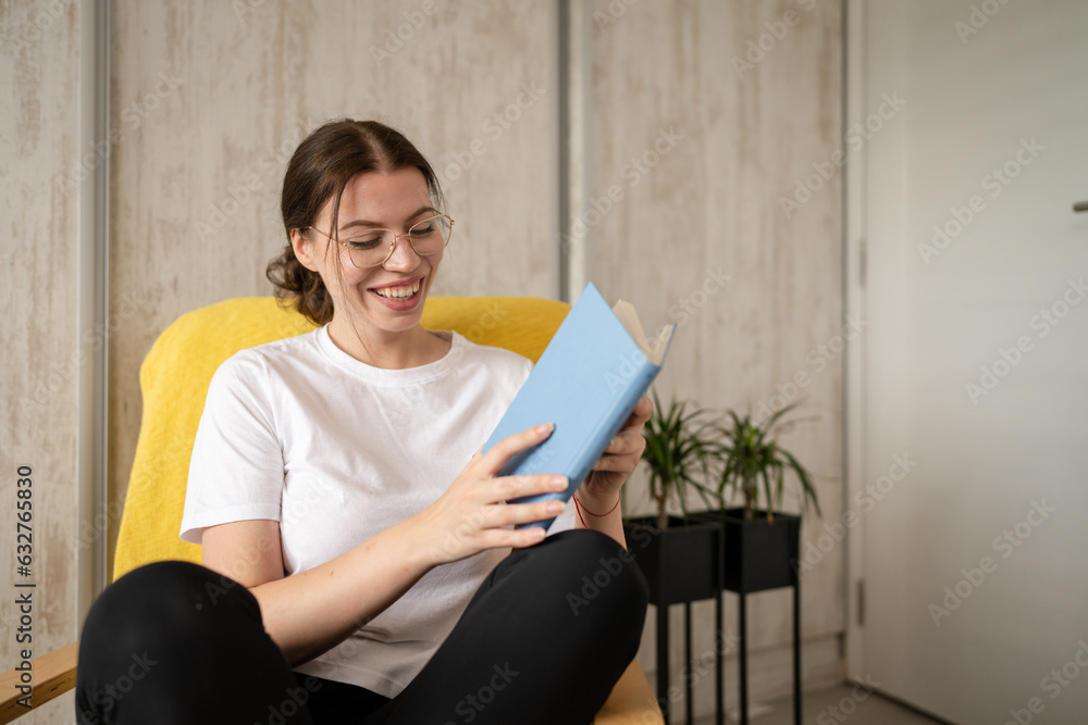 one woman young adult female read book while sitting in chair at home one woman young adult female read book while sitting in chair at home