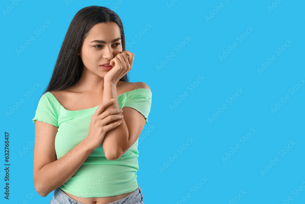 Beautiful young woman biting nails on blue background Beautiful young woman biting nails on blue background