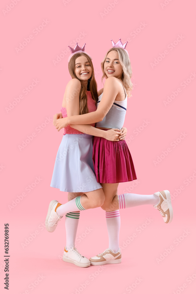 Young sisters in crowns hugging on pink background Young sisters in crowns hugging on pink background