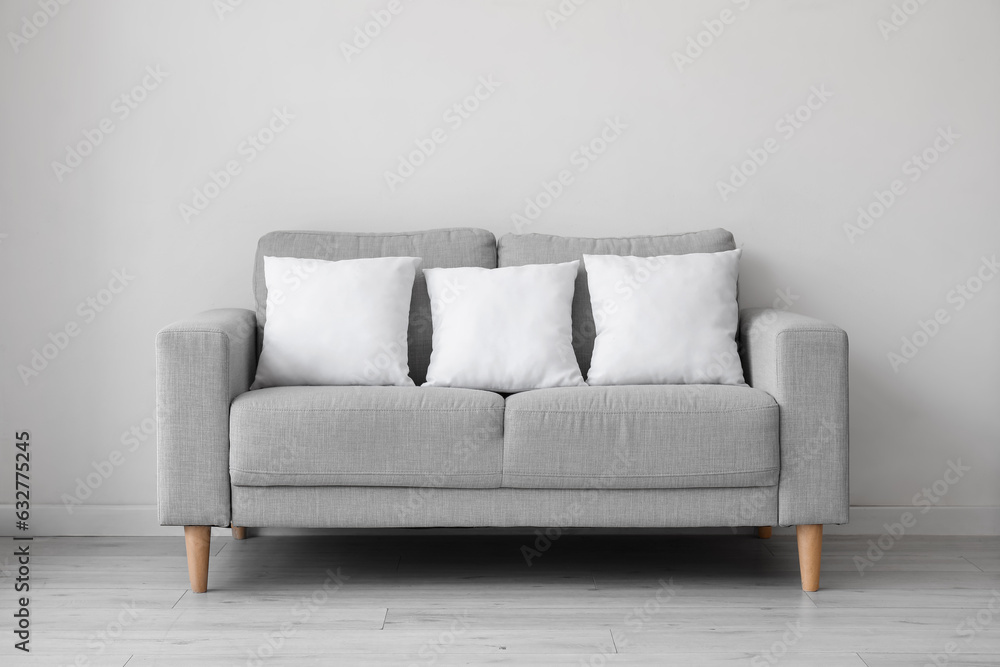 Fototapeta premium Grey sofa with pillows near white wall