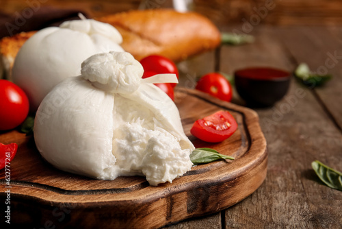 Board with tasty Burrata cheese on wooden background
