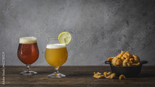 One Wheat and one brown ale, in Tulip glasses on wood table with bowl of pork rinds