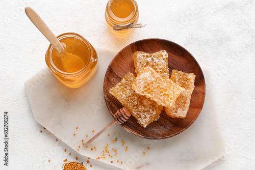 Jars of sweet honey and plate with combs on white background