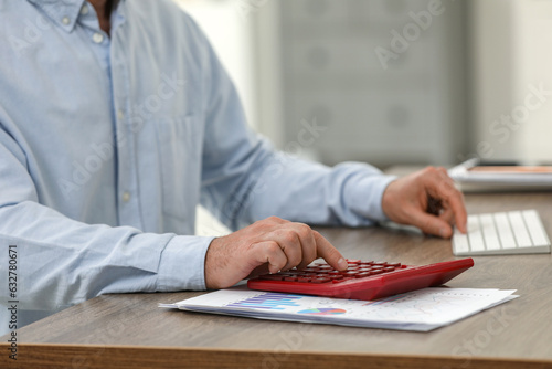 Professional accountant using calculator at wooden desk in office, closeup