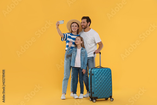 Happy family with suitcase taking selfie on orange background