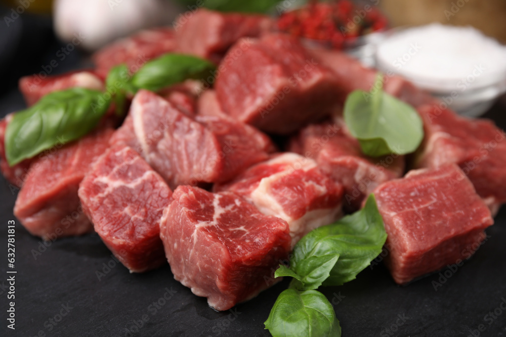 Cut fresh beef meat and basil leaves on slate plate, closeup