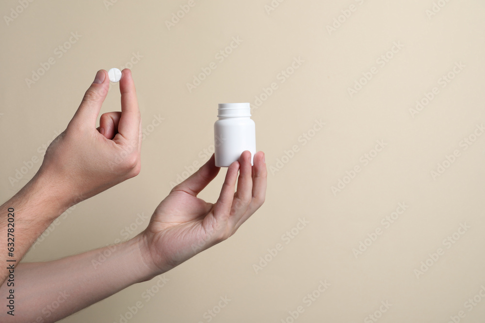 Man holding pill and bottle on beige background, closeup. Space for text Man holding pill and bottle on beige background, closeup. Space for text