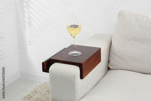 Foto Glass of white wine on sofa with wooden armrest table in room