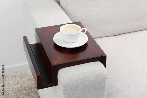 Cup of coffee on sofa with wooden armrest table indoors. Interior element photo