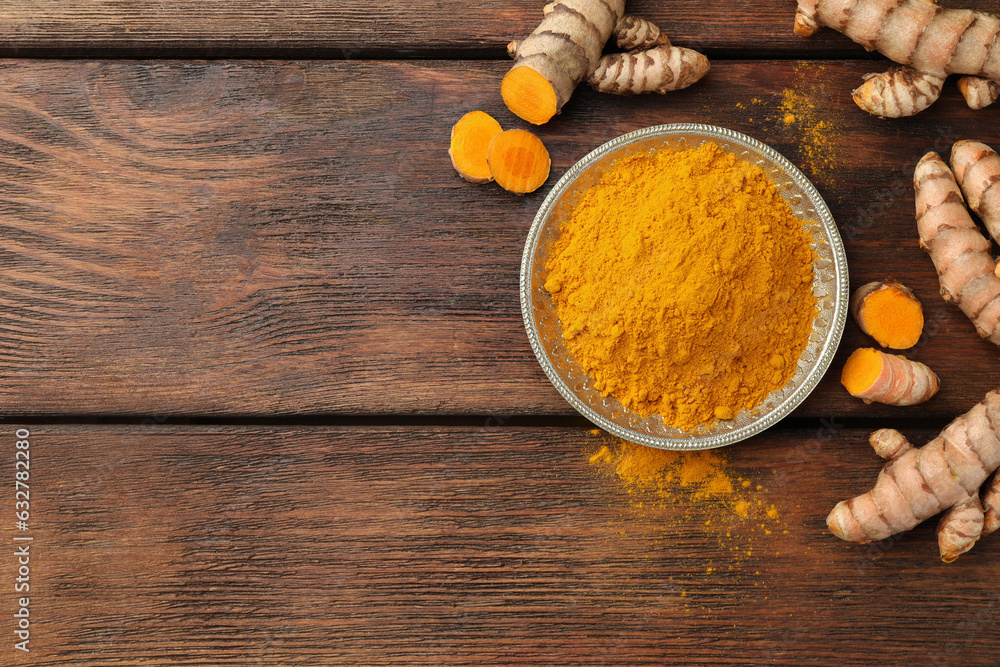 Plate with aromatic turmeric powder and cut roots on wooden table, flat lay. Space for text Plate with aromatic turmeric powder and cut roots on wooden table, flat lay. Space for text