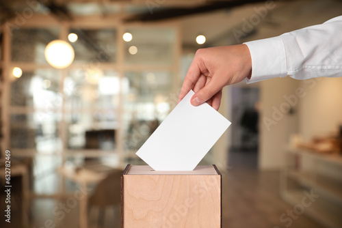 Man putting his vote into ballot box on blurred background, closeup