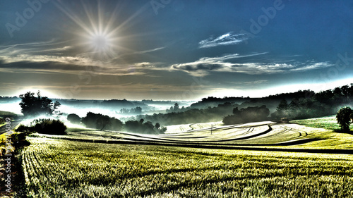A surrealistic sunrise in a rural area  as seen by the roadside overlooking the wheat field and the mist in the woods beyond  on a beautiful autumn morning