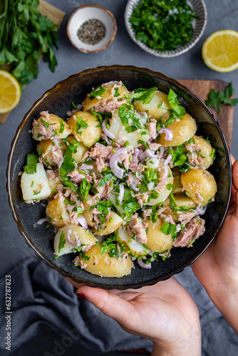 Hands holding a bowl of tuna potato salad photographed from top view. photo