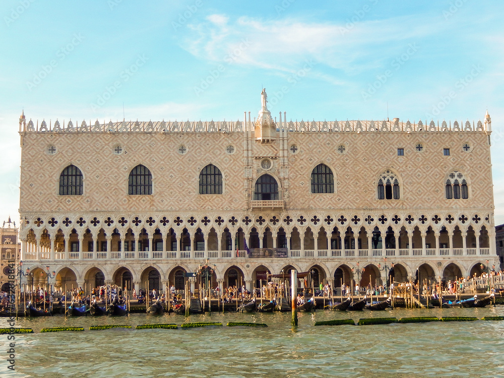 Historic Doge's Palace exterior with gondolas by sea is famous Venetian architecture with sunny sky in Venice in Italy
