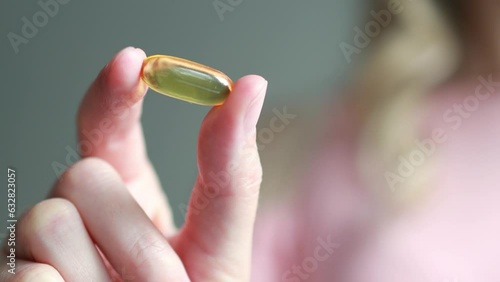 Close-up of a yellow capsule of omega-3 nutritional supplement or fish oil or vitamin D3 in a woman's palm