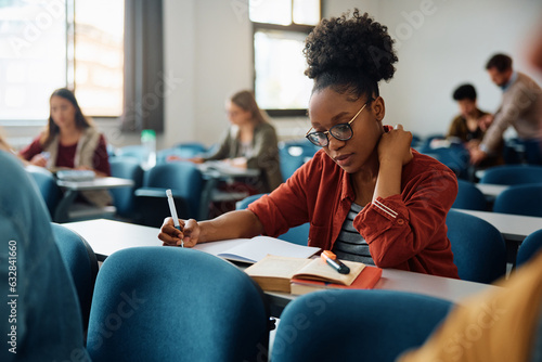Black female student takes notes while learning during class at lecture hall.