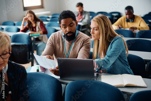 Black adult education teacher assists his student with an assignment during class in classroom.