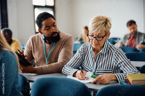 Mature woman studying with help of teacher during adult educational training class in lecture hall.