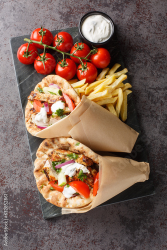 Greek gyros with chicken and fresh vegetables served with tzatziki sauce and french fries close-up on a board on the table. Vertical top view from above photo