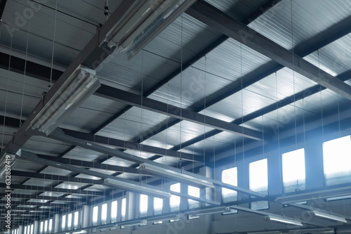 Under the roof, with the light from the outside come through the window, of a factory building with various structures and lines.