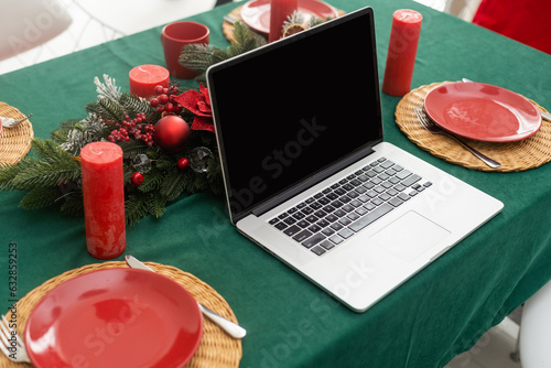 Celebrating merry christmas and new year at home, candles and garlands, a glass of champagne and a laptop on the table in the kitchen